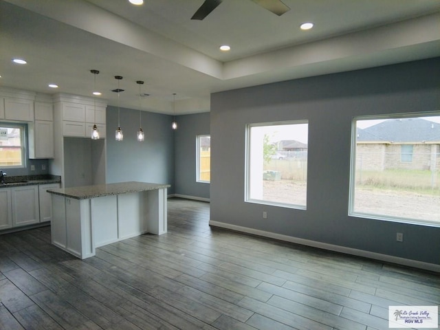 kitchen with sink, dark stone countertops, hanging light fixtures, white cabinets, and a kitchen island