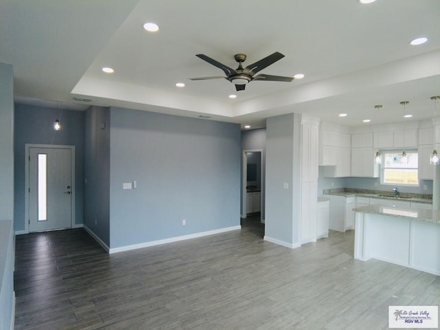 kitchen with pendant lighting, white cabinetry, hardwood / wood-style floors, light stone counters, and a raised ceiling