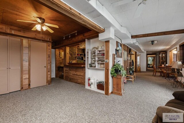 living room featuring beam ceiling, wooden walls, carpet floors, and ceiling fan