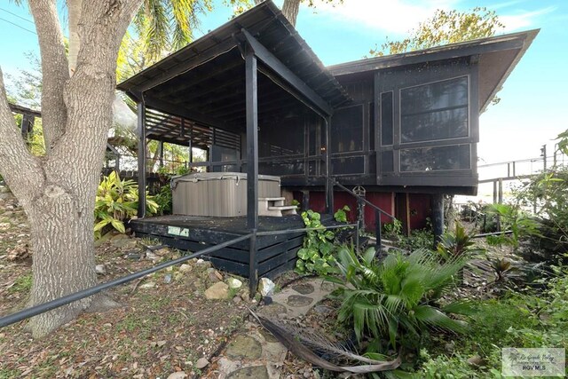 view of home's exterior with a hot tub and a sunroom