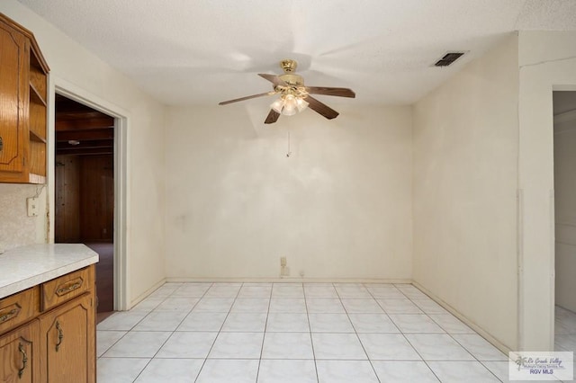 empty room featuring ceiling fan, light tile patterned flooring, and a textured ceiling