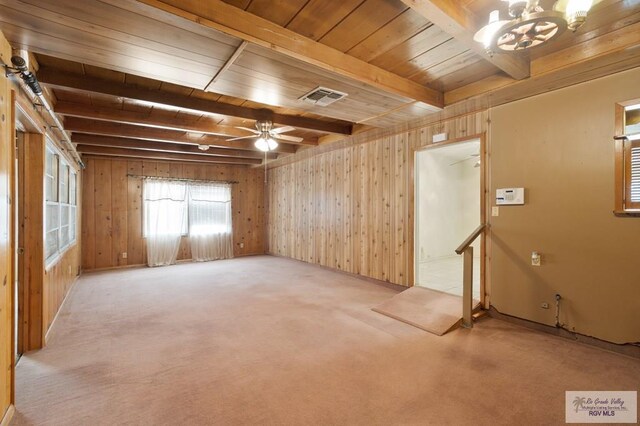 carpeted empty room featuring wood walls, beamed ceiling, and ceiling fan with notable chandelier