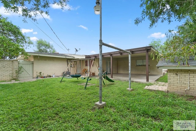 rear view of property with a gate, a patio area, fence, a yard, and brick siding