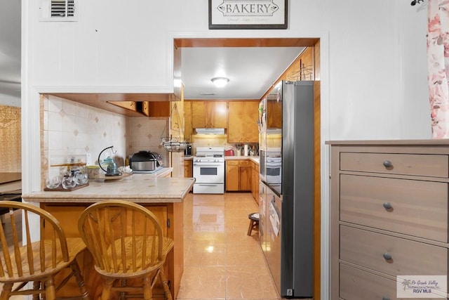 kitchen featuring freestanding refrigerator, decorative backsplash, under cabinet range hood, light countertops, and white gas range