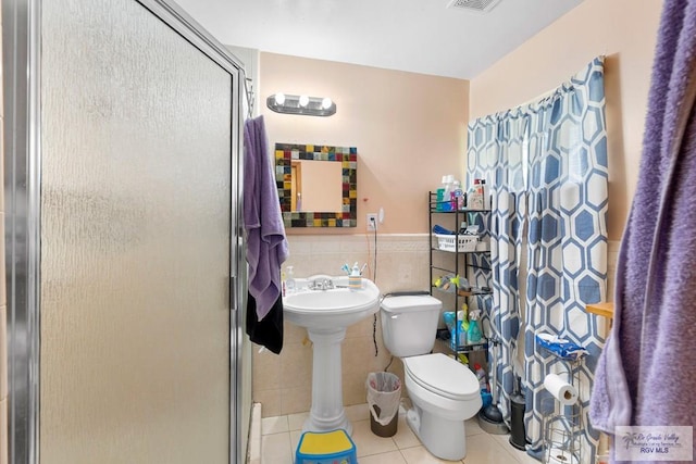 full bath featuring tile patterned floors, toilet, a stall shower, and tile walls