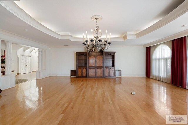 unfurnished living room featuring a tray ceiling, crown molding, an inviting chandelier, and light wood-type flooring