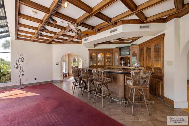 bar with beam ceiling, dark tile patterned flooring, ceiling fan, and coffered ceiling