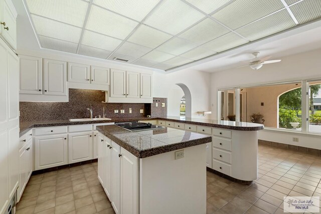 kitchen featuring white cabinets, ceiling fan, a kitchen island, kitchen peninsula, and stainless steel gas cooktop