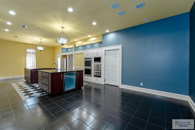 kitchen with appliances with stainless steel finishes, a kitchen island with sink, decorative light fixtures, an inviting chandelier, and wine cooler