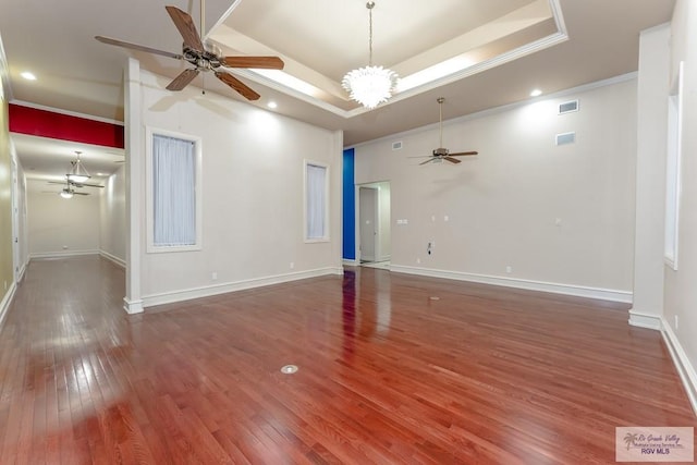 empty room featuring a raised ceiling, dark hardwood / wood-style flooring, an inviting chandelier, and crown molding