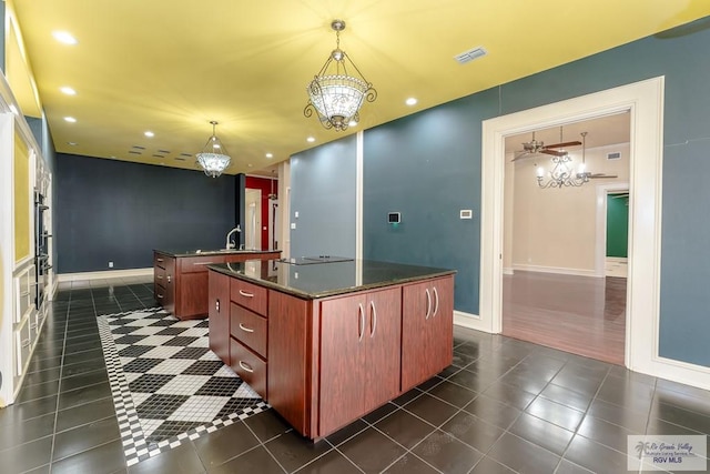 kitchen featuring an island with sink, pendant lighting, dark tile patterned flooring, and an inviting chandelier