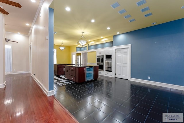 kitchen featuring appliances with stainless steel finishes, dark wood-type flooring, pendant lighting, wine cooler, and an island with sink