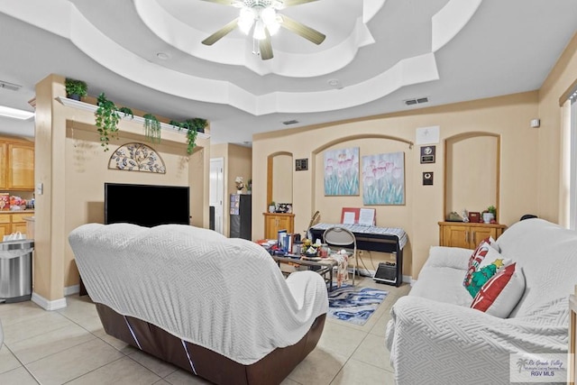 tiled living room with ceiling fan and a raised ceiling