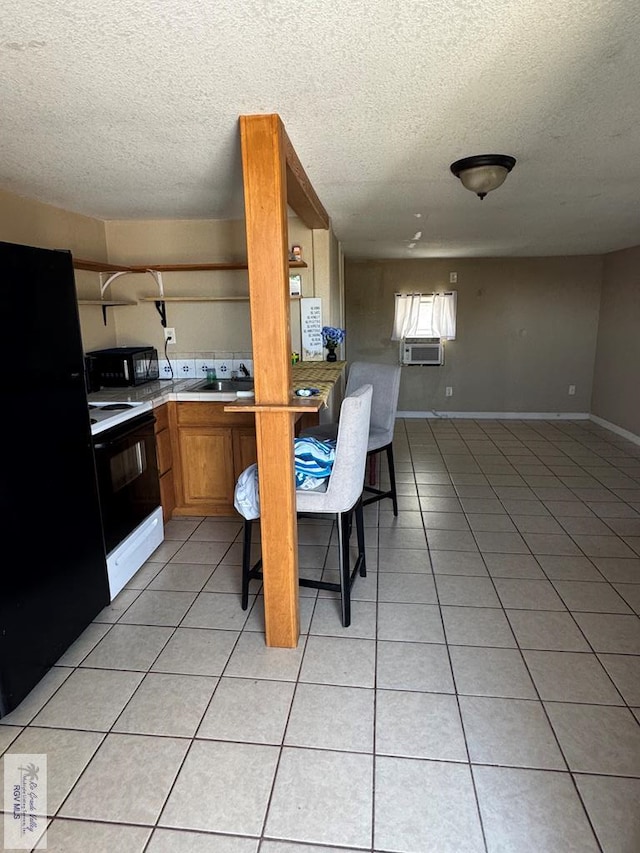 kitchen featuring black appliances, a kitchen breakfast bar, light tile patterned floors, and a textured ceiling