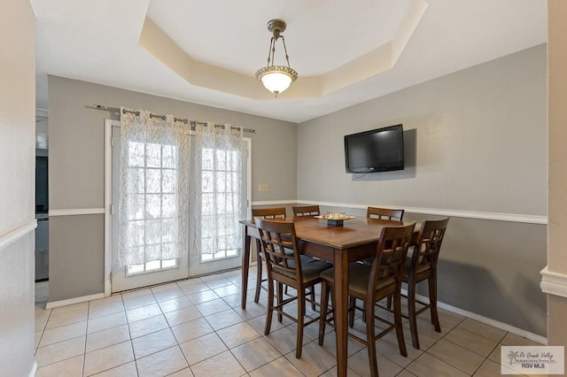 dining room with a tray ceiling and light tile patterned floors