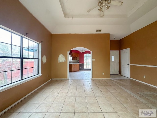 empty room with visible vents, a tray ceiling, light tile patterned floors, arched walkways, and a ceiling fan