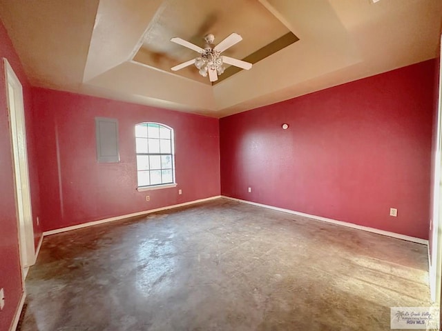 spare room featuring baseboards, a raised ceiling, concrete floors, and a ceiling fan