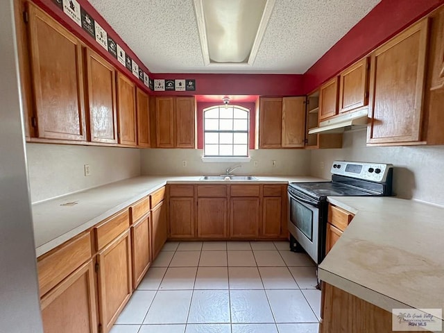 kitchen with under cabinet range hood, stainless steel electric stove, light countertops, brown cabinetry, and a sink