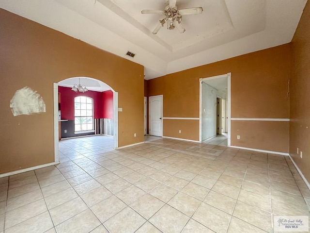 spare room with light tile patterned floors, baseboards, a tray ceiling, arched walkways, and ceiling fan with notable chandelier