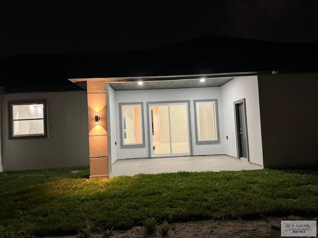 back of house at night featuring a patio area and stucco siding
