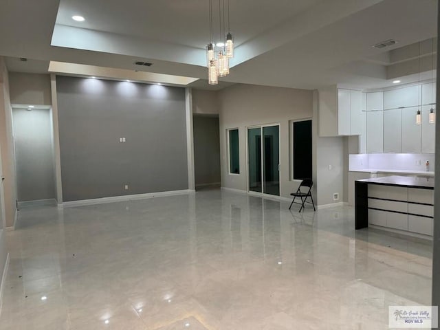 unfurnished living room featuring a notable chandelier, recessed lighting, baseboards, a tray ceiling, and visible vents