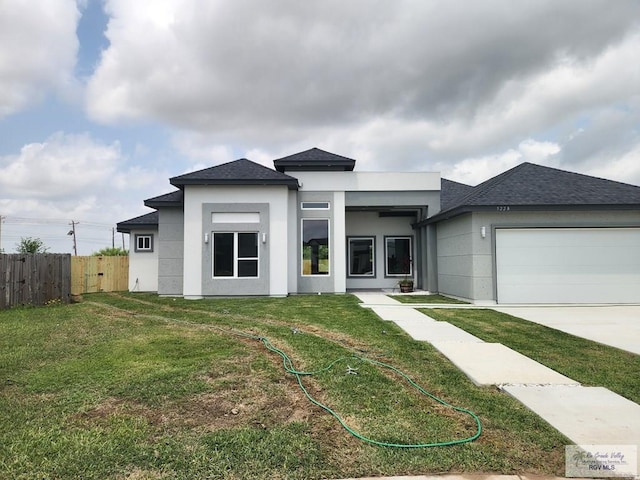 prairie-style home featuring an attached garage, fence, a front yard, and stucco siding
