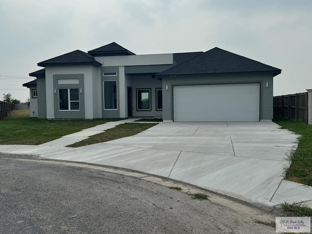 prairie-style home featuring a garage, fence, a front yard, stucco siding, and driveway