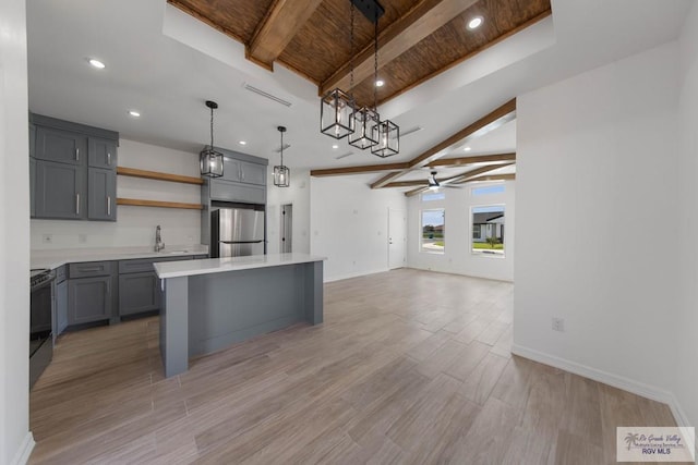 kitchen with stove, gray cabinetry, a kitchen island, ceiling fan, and stainless steel refrigerator