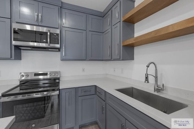 kitchen with stainless steel appliances, light stone counters, gray cabinetry, and sink