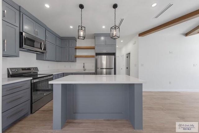 kitchen with beamed ceiling, gray cabinets, a kitchen island, and stainless steel appliances