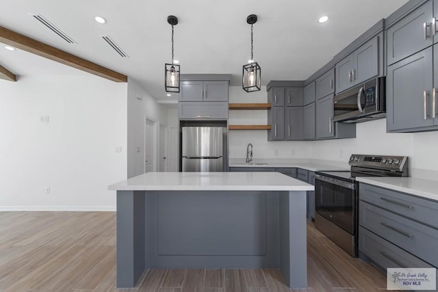 kitchen featuring beam ceiling, gray cabinetry, stainless steel appliances, pendant lighting, and a kitchen island