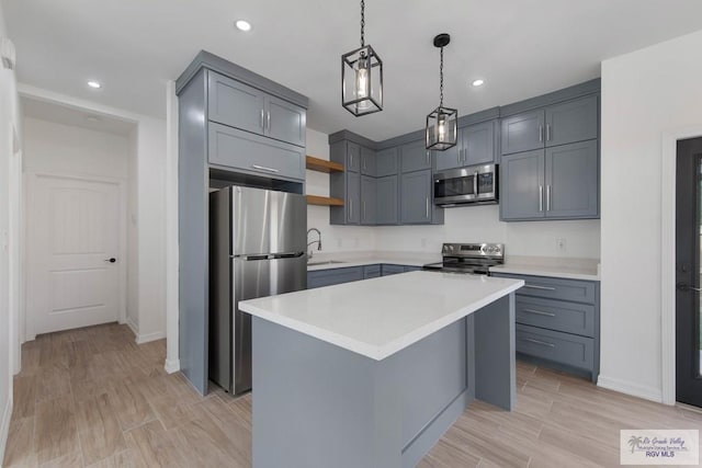 kitchen featuring gray cabinetry, sink, stainless steel appliances, decorative light fixtures, and a kitchen island