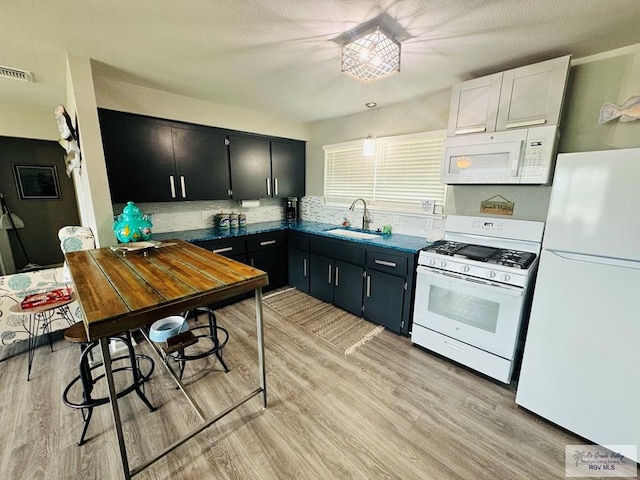 kitchen with white appliances, light hardwood / wood-style floors, hanging light fixtures, and sink