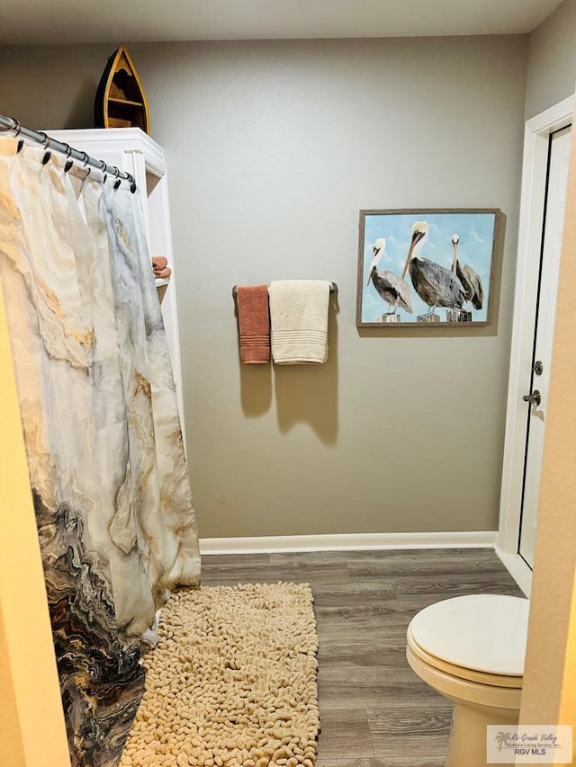 bathroom with hardwood / wood-style floors, a shower with curtain, and toilet