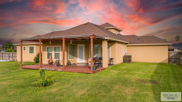 back house at dusk with central AC and a lawn