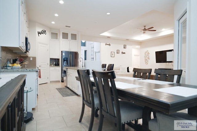 dining space with a raised ceiling, ceiling fan, sink, and light tile patterned floors