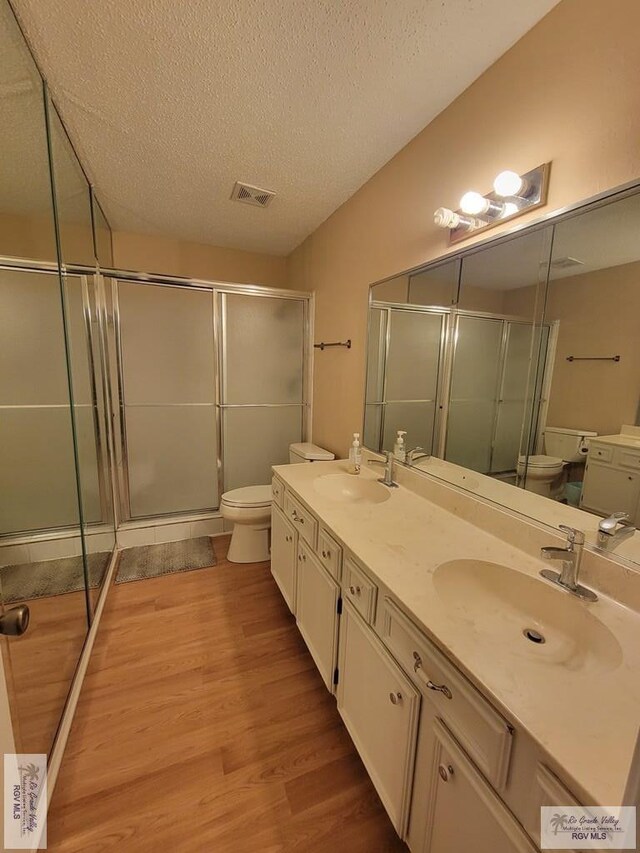 bathroom with vanity, toilet, a textured ceiling, an enclosed shower, and wood-type flooring