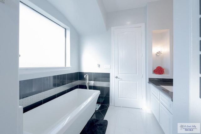 bathroom with tile patterned floors, a bathtub, vanity, and tile walls