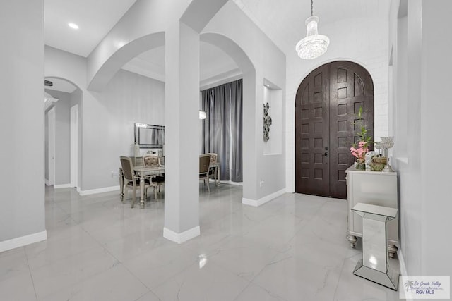 foyer featuring arched walkways, marble finish floor, an inviting chandelier, and baseboards