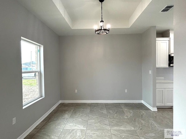 unfurnished dining area with an inviting chandelier and a tray ceiling