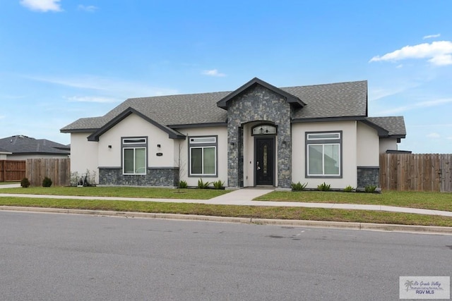 view of front of house with a shingled roof, stone siding, fence, and a front lawn