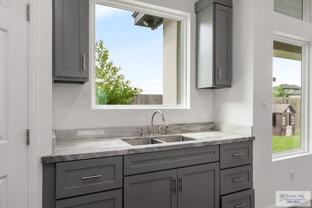 kitchen with a sink, gray cabinetry, and light stone countertops