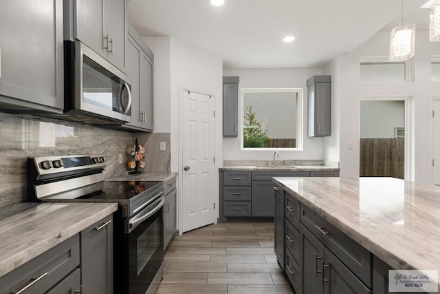 kitchen featuring stainless steel appliances, gray cabinets, decorative backsplash, a sink, and light stone countertops