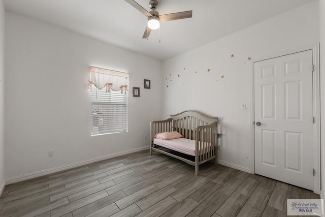 bedroom with a crib, wood finished floors, a ceiling fan, and baseboards