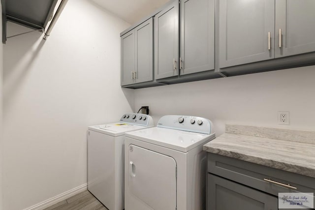 laundry room with baseboards, cabinet space, light wood-style flooring, and washing machine and clothes dryer