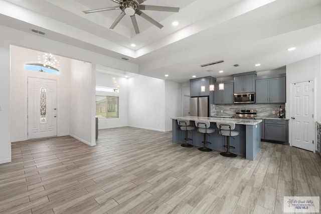 kitchen featuring visible vents, appliances with stainless steel finishes, a breakfast bar area, light wood-style floors, and backsplash