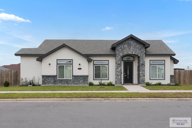 view of front of property with fence, stone siding, roof with shingles, stucco siding, and a front yard