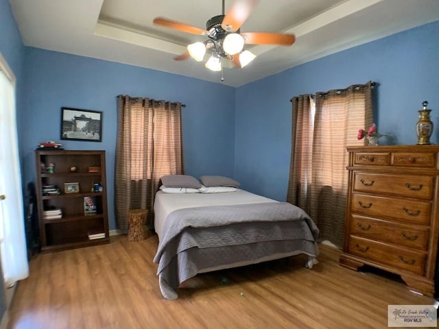 bedroom featuring a tray ceiling, ceiling fan, and light hardwood / wood-style floors