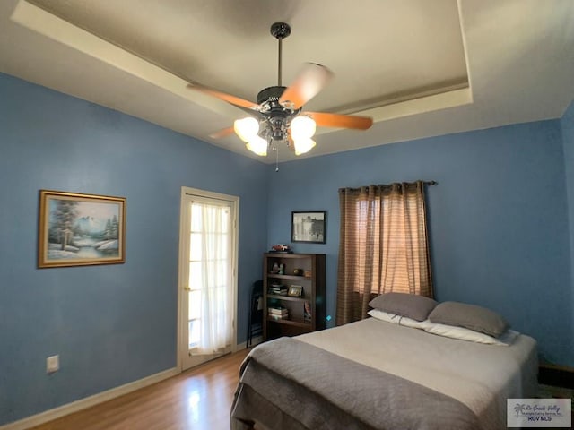 bedroom with a raised ceiling, ceiling fan, and hardwood / wood-style flooring