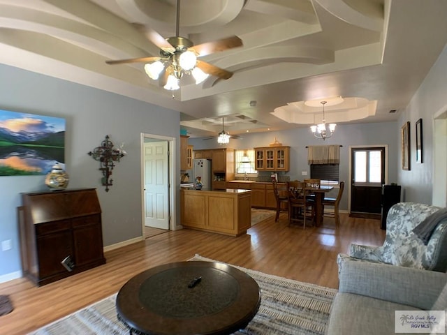 living room featuring a raised ceiling, light hardwood / wood-style flooring, ceiling fan with notable chandelier, and sink